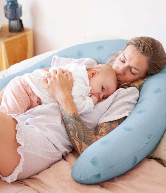 A woman lying with her little one on the bed comfortably over a pregnancy pillow