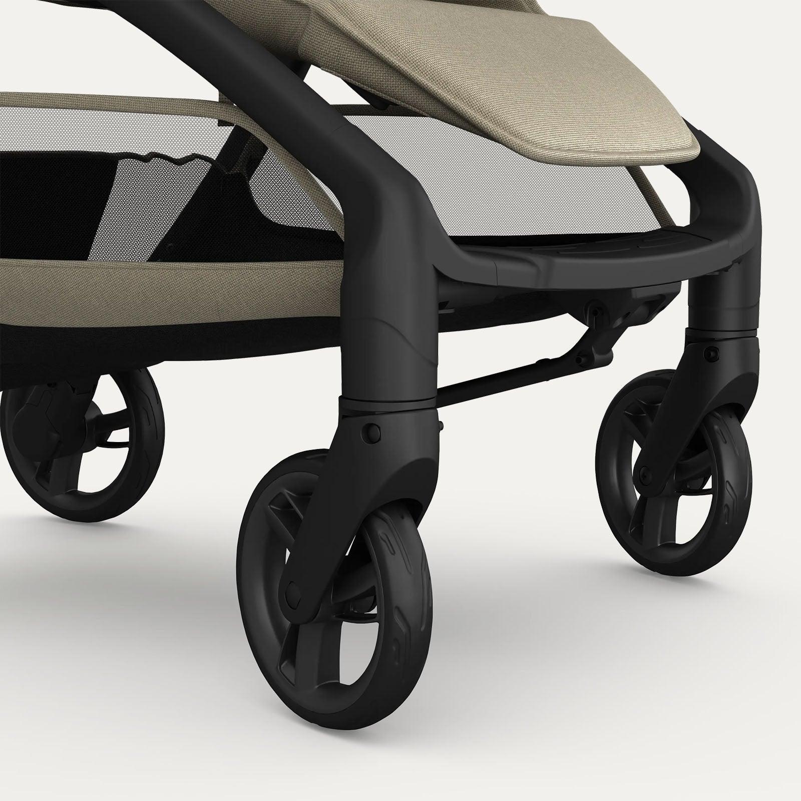 Close-up view of the front wheels of the taupe-colored Redsbaby Aeron stroller with a black frame. The image highlights the no-puncture wheels and suspension system designed for rough terrain, as well as part of the stroller's footrest and mesh storage basket. Close-up view of the front wheels of the taupe-colored Redsbaby Aeron stroller with a black frame. The image highlights the no-puncture wheels and suspension system designed for rough terrain, as well as part of the stroller's footrest and mesh storage basket.