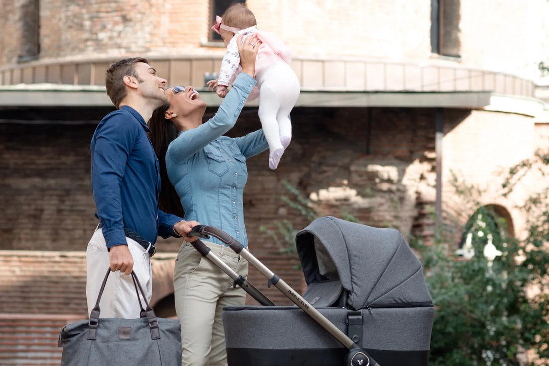 A joyful couple is outdoors with their baby and a Cangaroo Macan 2in1 Stroller. The mother lifts the baby in the air playfully while the father looks on affectionately, with the stroller's carrycot attached to the chassis.