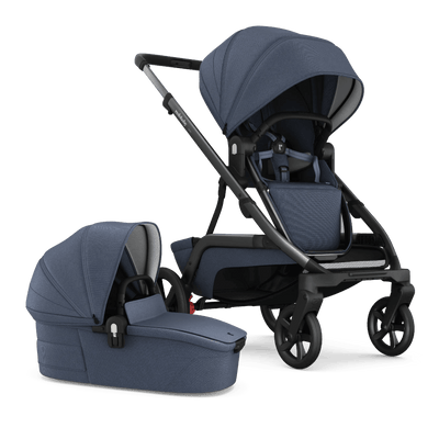 A side-by-side image of the Redsbaby NUVO stroller in blue slate color, featuring both the pram and bassinet attachments. The pram on the left has a sleek, ergonomic design with a curved handle and a reclining seat with a secure five-point harness system, while the bassinet on the right showcases a protective hood and a flat sleeping surface, both made with textured, high-quality fabric. The stroller demonstrates its versatility with easy-to-attach modules for different stages of a baby's development.