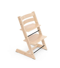 A natural wood Tripp Trapp high chair with adjustable seat and footplate, featuring a minimalist design with three horizontal backrest slats and a sturdy base, accented with black metal supports, against a white background.