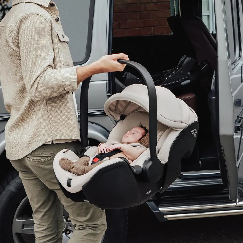 Father carrying the Britax Römer Baby-Safe Pro Lux Infant Car Seat in Taupe with newborn inside, showcasing its portable design and convenience for travel in a car.