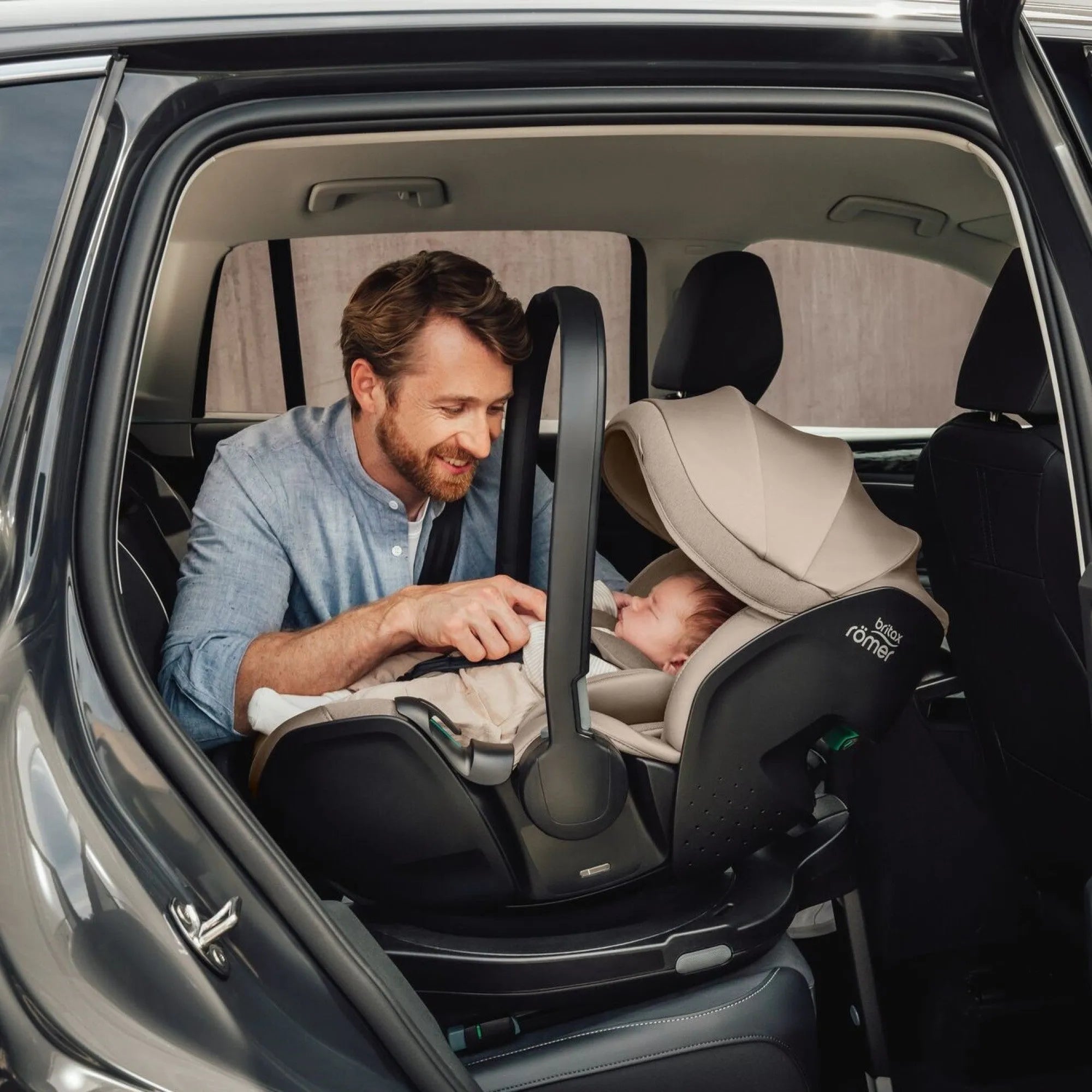 Father adjusting the Britax Römer Baby-Safe Pro Lux Infant Car Seat in Taupe for his newborn in the backseat of a car, demonstrating ease of installation and comfort for the baby.