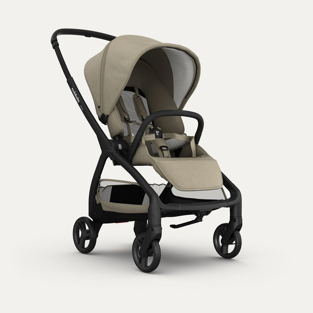 A taupe-colored Redsbaby Aeron stroller with a sleek black frame. The stroller features a canopy, a comfortable seat with a harness, a footrest, and a spacious storage basket underneath. It is designed with four wheels for easy maneuverability and a minimalist, modern aesthetic.